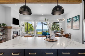 A modern kitchen with a large island, pendant lights, and a view to the outdoors. - Luxury Lakefront Home! Private Beach & Perfect for Entertaining! (Two Rivers)