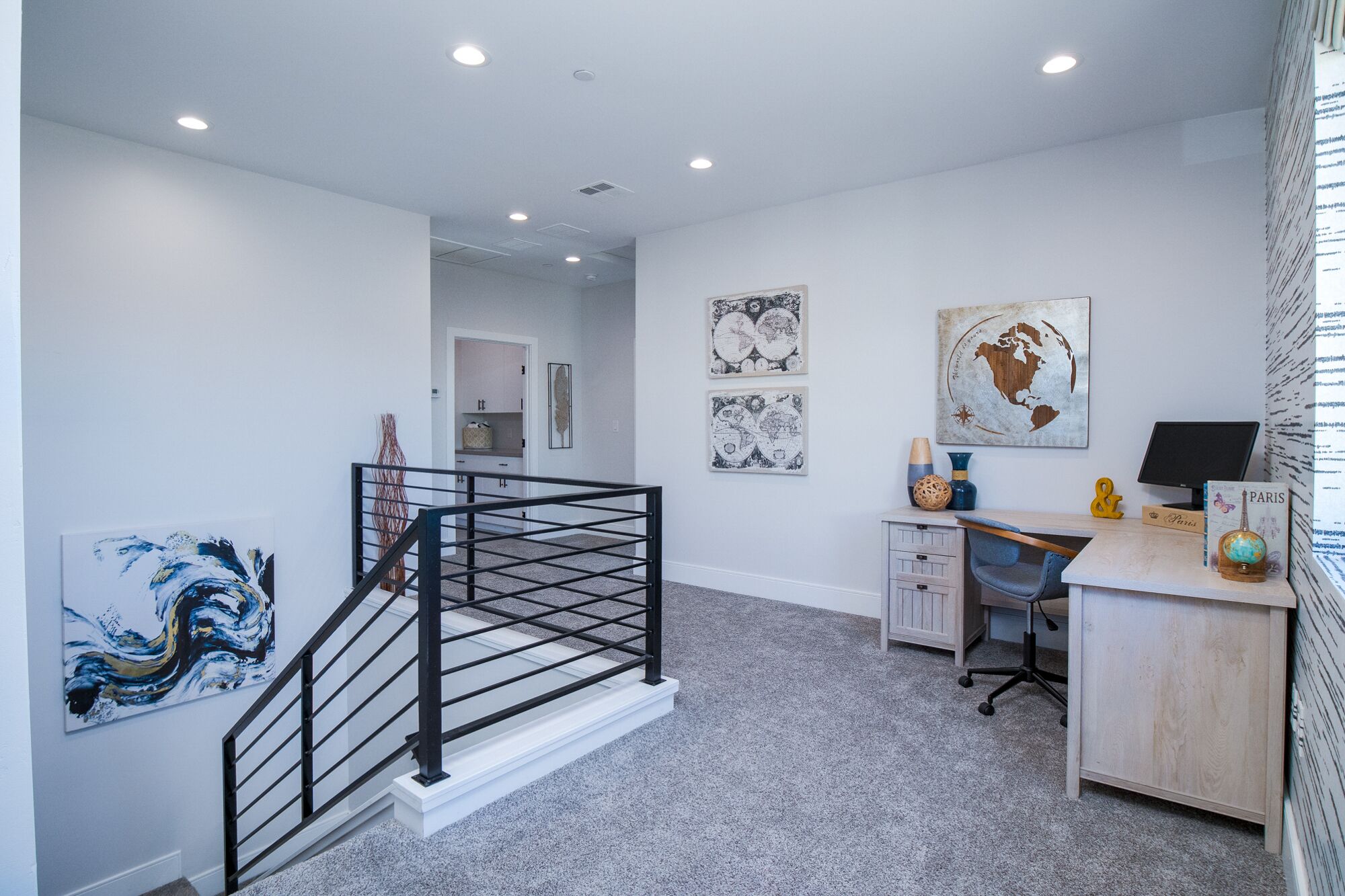 A modern office space with a staircase, desk, and artwork on the walls.