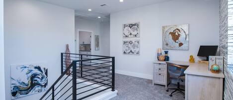 A modern office space with a staircase, desk, and artwork on the walls.