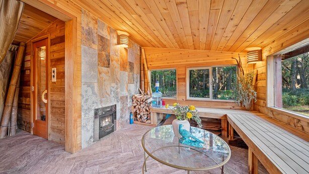 A wooden cabin interior with a glass table, benches, a fireplace, and a stone wall. - River Retreat RV Campground ~ Gym / Game Room / Sauna (Jacksonville)