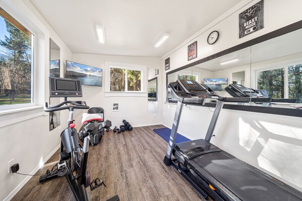 Et fitnesscenter med træningsudstyr, løbebånd, motionscykler og et tv-skærm.