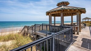 Ein hölzerner Strandpavillon mit Dach, einer Holzterrasse und einem Geländer.