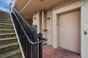 A wooden staircase with a metal handrail leading to a beige door. - Afternoon Delight-Oceanfront Condo, Pet Friendly, Community Pools (Kill Devil Hills)