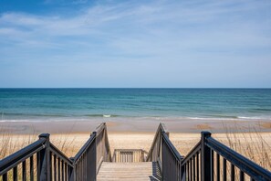 A wooden boardwalk leading to a sandy beach with a clear view of the ocean.