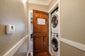 A laundry room with a wooden door, a wall-mounted thermostat, and two front-loading washing machines. - Afternoon Delight-Oceanfront Condo, Pet Friendly, Community Pools (Kill Devil Hills)