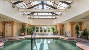 Una piscina interior con techo de cristal, plantas en macetas y una puerta con letrero de salida.