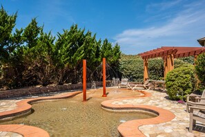 Uma área externa ajardinada com um espelho d'água, assentos e um pérgola.