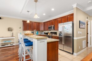 A modern kitchen with wooden cabinets, stainless steel appliances, a central island with bar stools, and a hanging pendant light.
