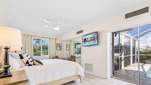 Un dormitorio con cama, televisión, ventilador de techo, ventana y puerta corrediza de vidrio que da a una zona de piscina.