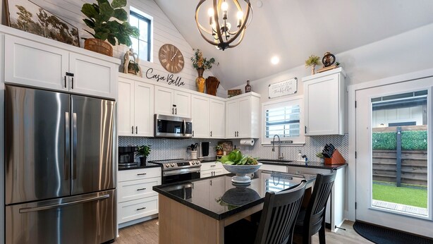 A modern kitchen with stainless steel appliances, a herringbone backsplash, and a central island with bar stools.