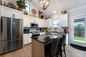 A modern kitchen with stainless steel appliances, a herringbone backsplash, and a central island with bar stools. - Casa Bella | Brand New Luxury Suite (Fredericksburg)