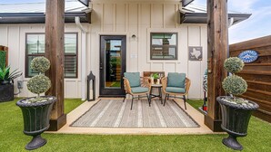 A house with a covered porch, two chairs, a small table, and decorative plants.