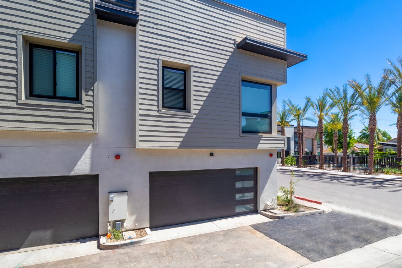 Un immeuble résidentiel moderne à deux étages, doté d’un garage, de grandes fenêtres et d’une pelouse bien entretenue agrémentée de palmiers.