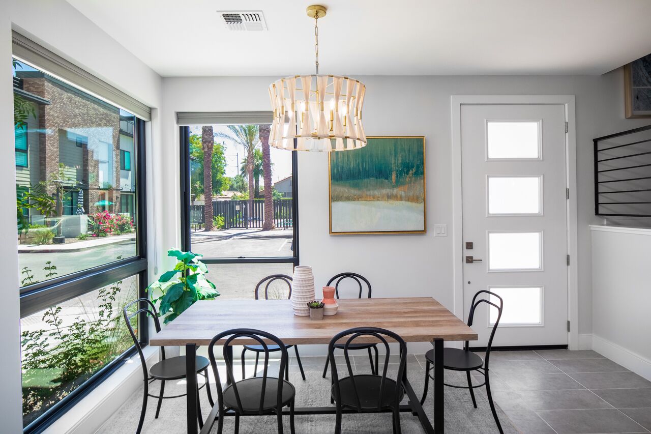 A dining area with a wooden table, black chairs, a hanging light fixture, and a painting on the wall.