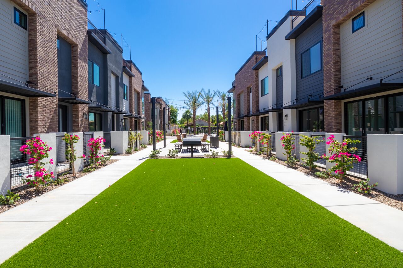 A row of modern townhouses with a central lawn and outdoor seating area.