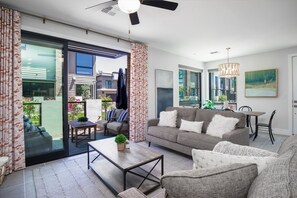 Uma sala de estar moderna com um sofá cinza, uma mesa de centro de madeira e um espaço de jantar com mesa e cadeiras.