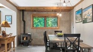 A cozy dining area with a wooden table and chairs, a stone fireplace, and a window with a view of greenery. - Deck with Private Hot Tub - Updated Townhome Overlooking Gore Creek + Parking for 4 (Vail)