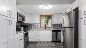 A modern kitchen with white cabinets, stainless steel appliances, and a patterned backsplash. - Deck with Private Hot Tub - Updated Townhome Overlooking Gore Creek + Parking for 4 (Vail)