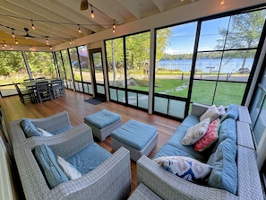 Une pièce spacieuse, meublée de mobilier en osier, dotée de grandes fenêtres et offrant une vue sur un lac.