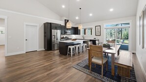 A modern kitchen with dark cabinetry, a central island, and bar stools. - Clark Fork Crossing - Adventures You Seek in Western Montana.  River access.  (Superior)