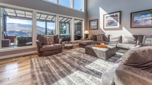 A spacious living room with large windows, a sectional sofa, a coffee table, and a rug. - Riverview Pool Villa near Chelan, and Hot Tub! (Chelan)