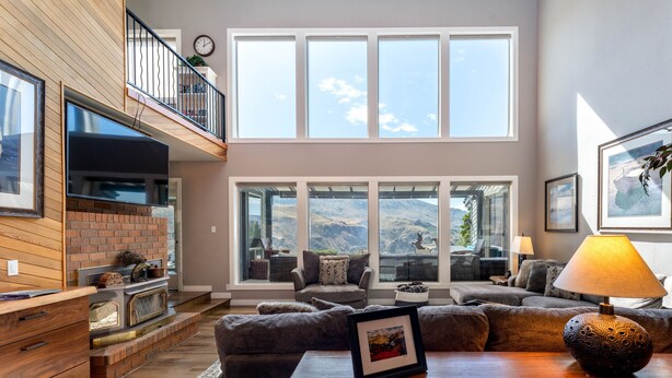 A spacious living room with a fireplace, large windows, and a view of the mountains. - Riverview Pool Villa near Chelan, and Hot Tub! (Chelan)