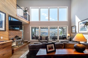 A spacious living room with a fireplace, large windows, and a view of the mountains. - Riverview Pool Villa near Chelan, and Hot Tub! (Chelan)