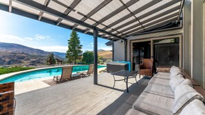 A covered outdoor area with a pool, lounge chairs, and a view of the mountains. - Riverview Pool Villa near Chelan, and Hot Tub! (Chelan)
