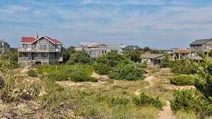 Un quartier résidentiel situé sur la côte, où les maisons présentent un mélange de styles architecturaux, le tout étant entouré d’une végétation luxuriante et surplombé d’un ciel dégagé.