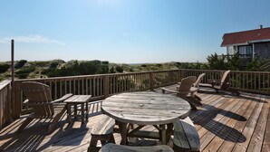 A wooden deck with a round table and chairs, overlooking a landscape with hills and a building in the background. - Oceanfront, Amazing Sunrises, Dog Friendly, Private deck & Screened in Porch (Avon)
