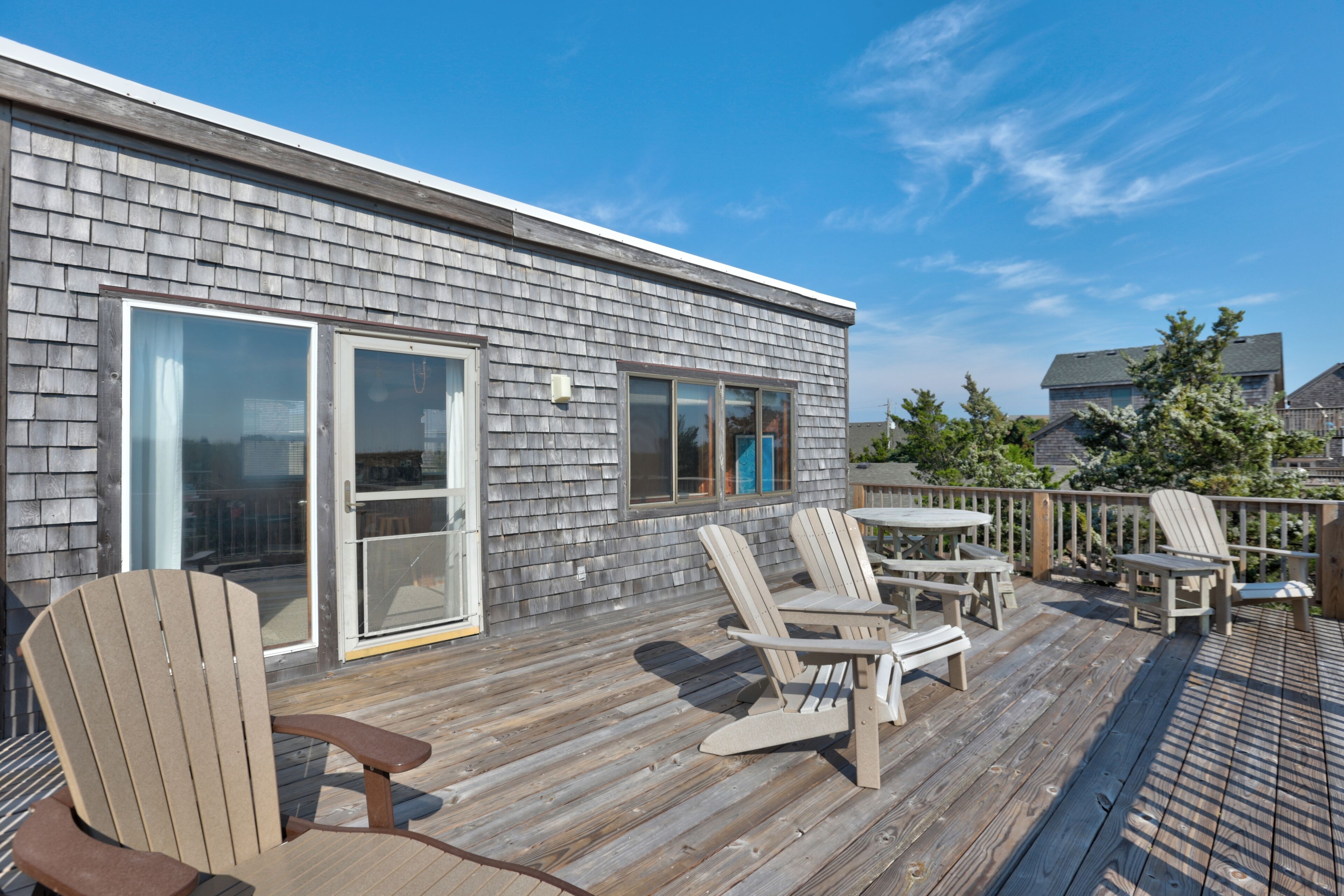Una terraza de madera con sillas Adirondack y una mesa, con vistas a un barrio residencial.
