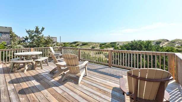 A wooden deck with picnic tables and chairs, overlooking a hilly landscape. - Oceanfront, Amazing Sunrises, Dog Friendly, Private deck & Screened in Porch (Avon)