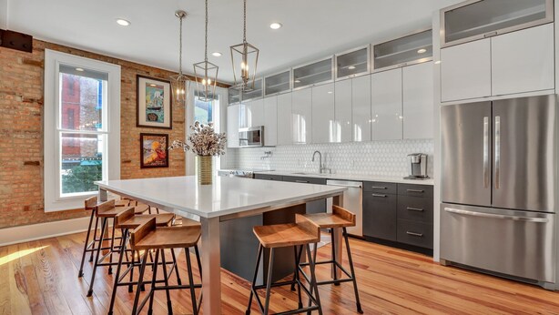 A modern kitchen with a large island, bar stools, stainless steel appliances, and a view through a large window. - Modern Broughton Loft with Southern Charm (Savannah)
