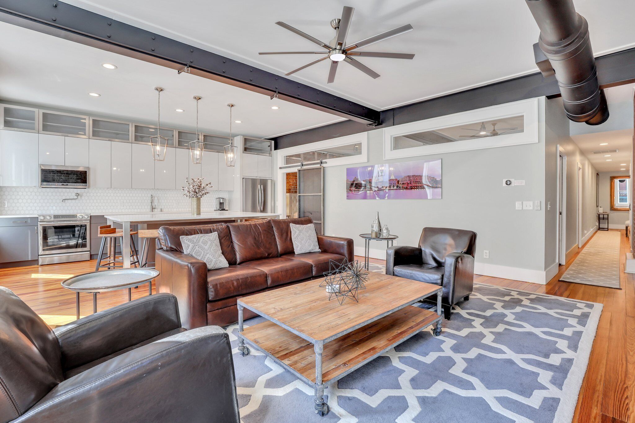 A spacious living area with a brown leather couch, a wooden coffee table, and a patterned rug.