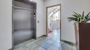 A hallway with a metallic elevator, a staircase, and a potted plant. - Modern Broughton Loft with Southern Charm (Savannah)