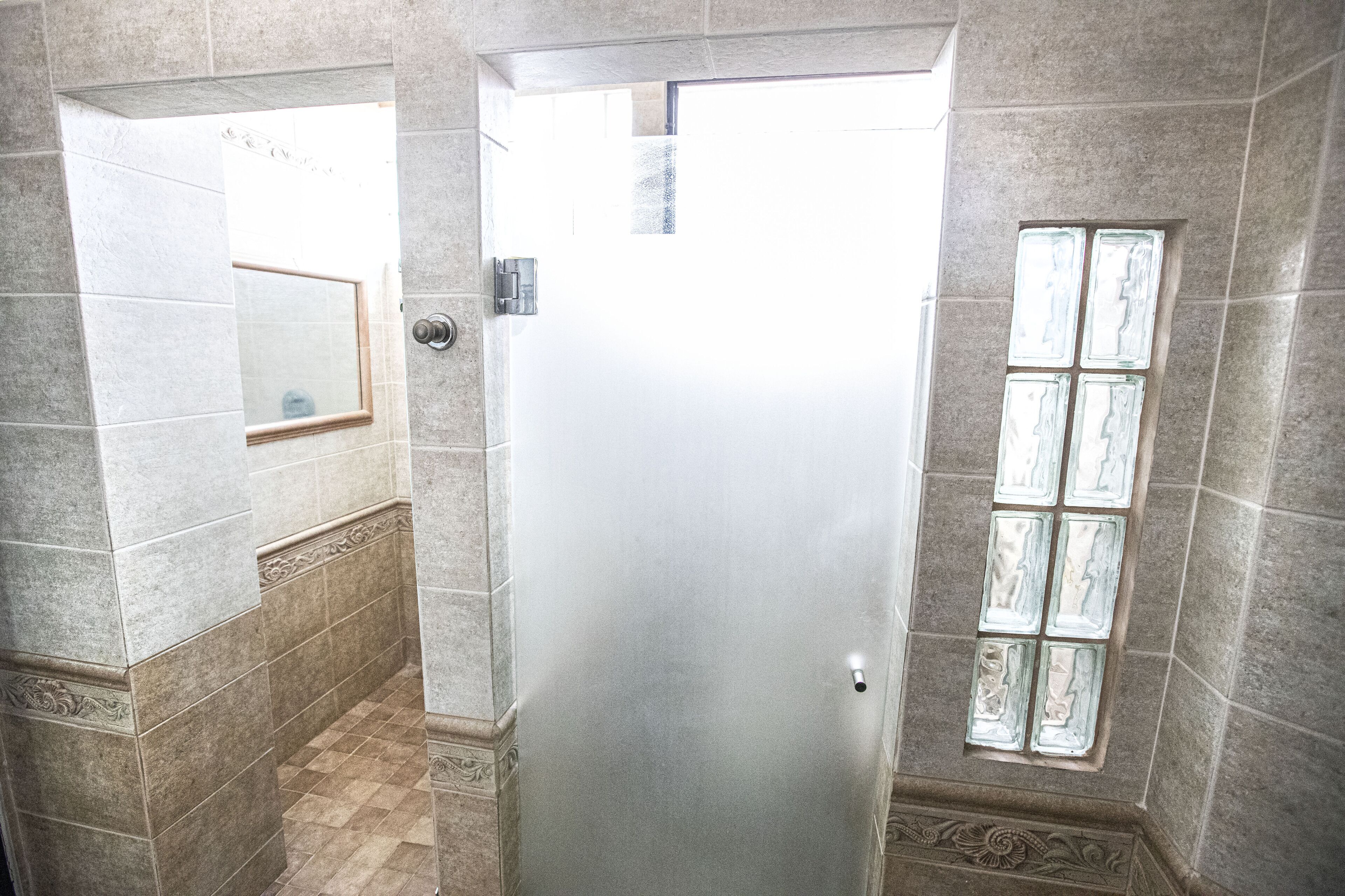 Une salle de bain avec une porte en verre dépoli, des murs carrelés, un miroir et une fenêtre avec des vitres en verre dépoli.