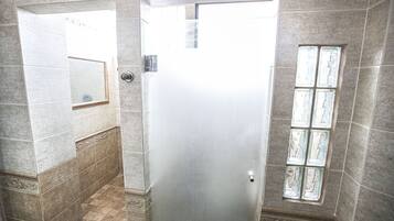 Une salle de bain avec une porte en verre dépoli, des murs carrelés, un miroir et une fenêtre avec des vitres en verre dépoli.