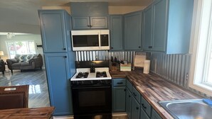 A compact kitchen with blue cabinets, a microwave, a stove, and a sink. - Blue Mountain Retreat (Elgin)