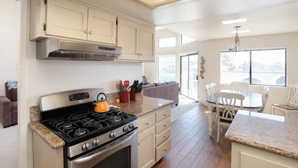 A kitchen with a stove, cabinets, and a dining area with chairs and a table.