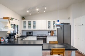 Una cocina moderna con armarios blancos, una isla central, horno empotrado y refrigerador de acero inoxidable.