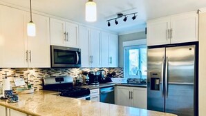 A modern kitchen with white cabinets, a stainless steel refrigerator, a microwave, and a granite countertop. - Your home away from home (Nassau)