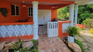 Uma casa com fachada vermelha, colunas brancas e varanda coberta com cerca branca.