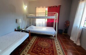A room with two bunk beds, a patterned rug, a nightstand with a lamp, and a window with curtains. - Mandarin Vacation Villa 2 Bedrooms - Toco (Toco)