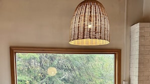 A room with a large window, a wicker pendant light, a white leather sofa, and a small round table.