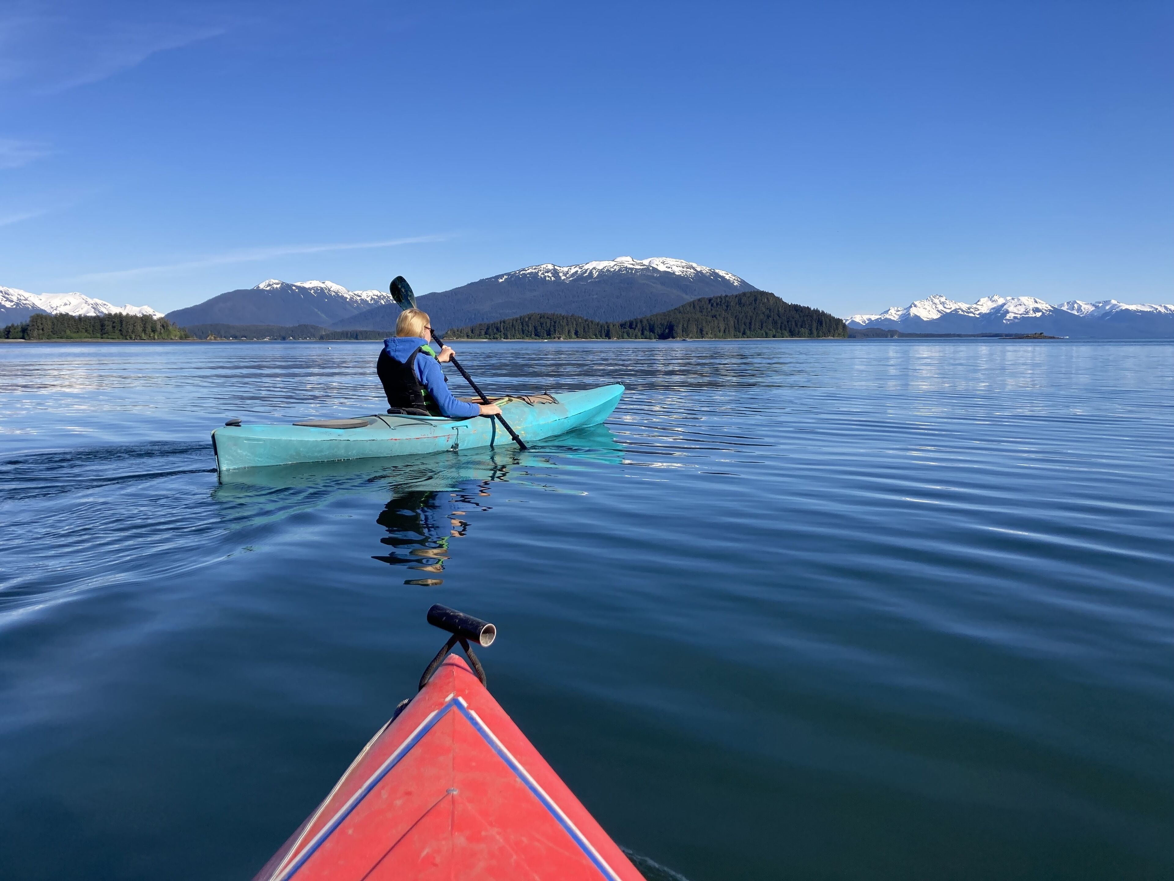 A person in a blue kayak on calm water with a mountainous landscape in the background.