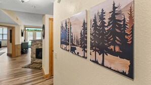 A hallway with wooden flooring, a stone fireplace, and three framed forest-themed wall art pieces.