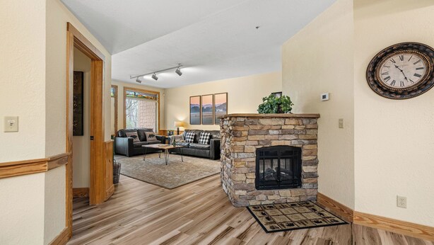 A living room with a stone fireplace, a sofa set, and a large clock on the wall.