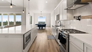 A modern kitchen with white cabinetry, a central island, and a dining area with a view. - Spokane Dream (Spokane County)