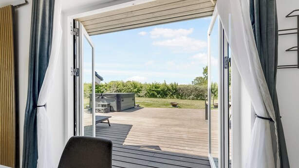 An open sliding door to an outdoor deck with a view of a grassy area and a building in the background. - New and modern holiday home with hot tub (Frørup)