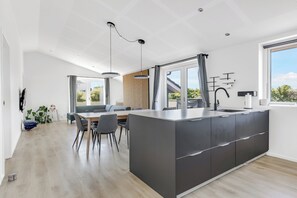 A modern kitchen with a large island, dining area with chairs, and a view through large windows.